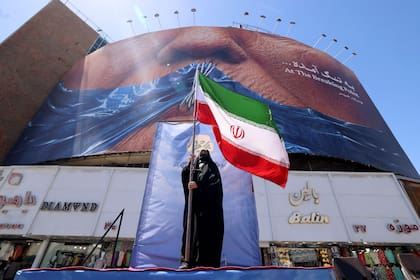 Una mujer sostiene la bandera iraní frente a una valla publicitaria antiestadounidense que hace referencia al presidente Donald Trump