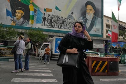 Una mujer iraní cruza una calle por el centro de Teherán, de fondo un mural en apoyo al Régimen